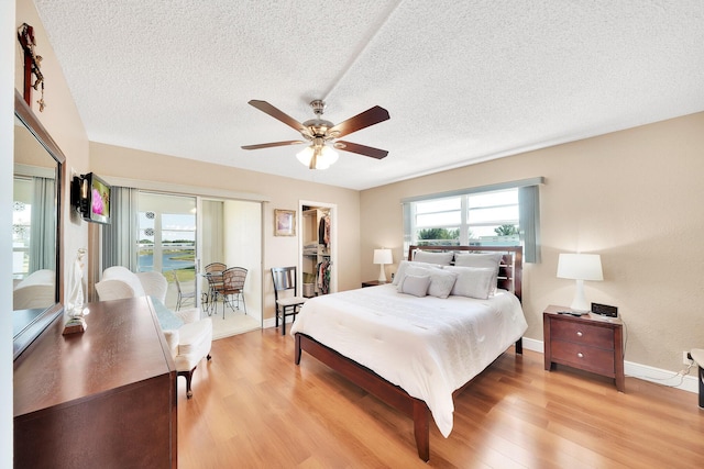 bedroom with a textured ceiling, ceiling fan, a spacious closet, light hardwood / wood-style floors, and a closet