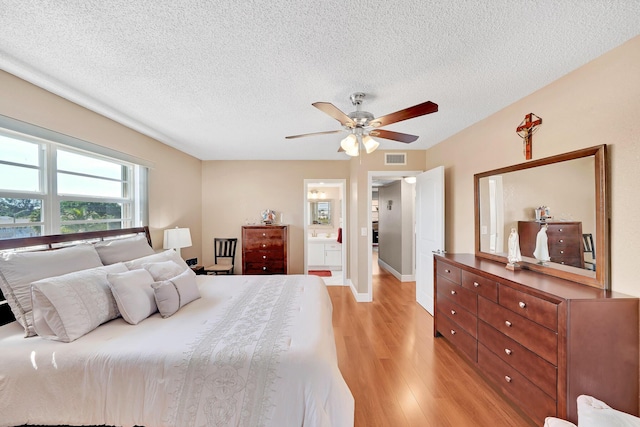 bedroom with ceiling fan, light hardwood / wood-style floors, a textured ceiling, and connected bathroom