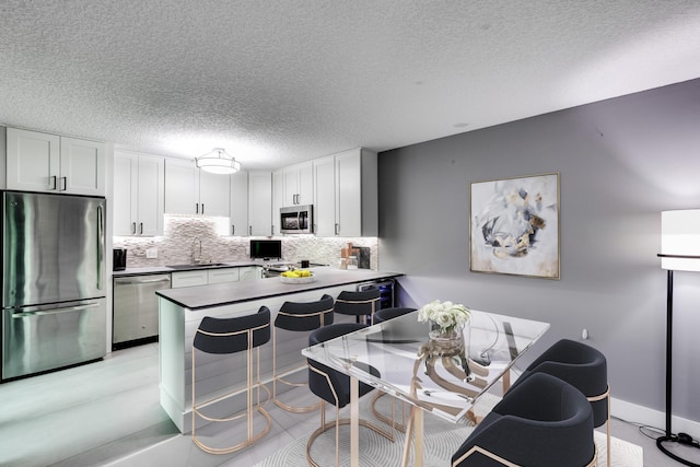 kitchen with white cabinetry, kitchen peninsula, appliances with stainless steel finishes, a breakfast bar, and sink