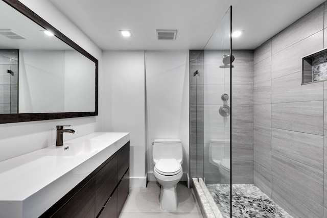 bathroom with toilet, tile patterned flooring, tiled shower, and vanity