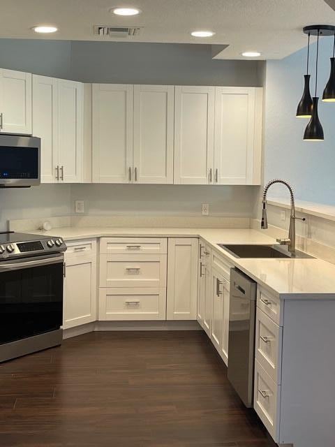 kitchen with appliances with stainless steel finishes, sink, dark hardwood / wood-style floors, white cabinetry, and hanging light fixtures