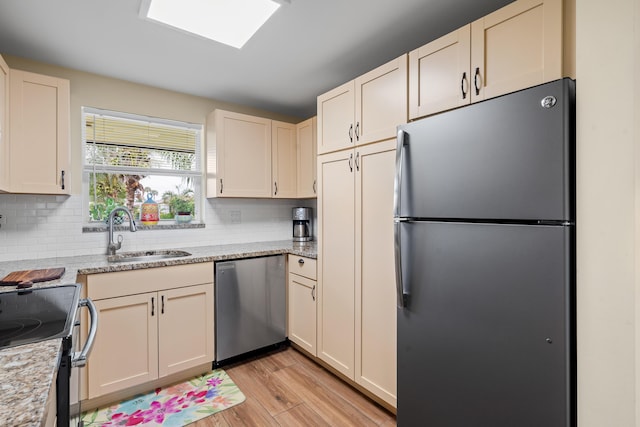 kitchen with sink, light stone counters, light hardwood / wood-style floors, decorative backsplash, and appliances with stainless steel finishes