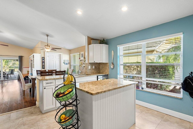 kitchen featuring sink, a kitchen island, light stone counters, vaulted ceiling, and white cabinets