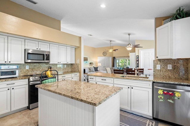 kitchen with appliances with stainless steel finishes, tasteful backsplash, ceiling fan, white cabinets, and a center island