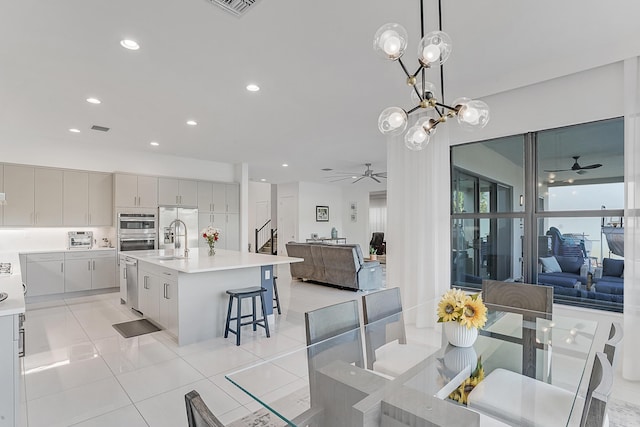 tiled dining space featuring ceiling fan with notable chandelier and sink