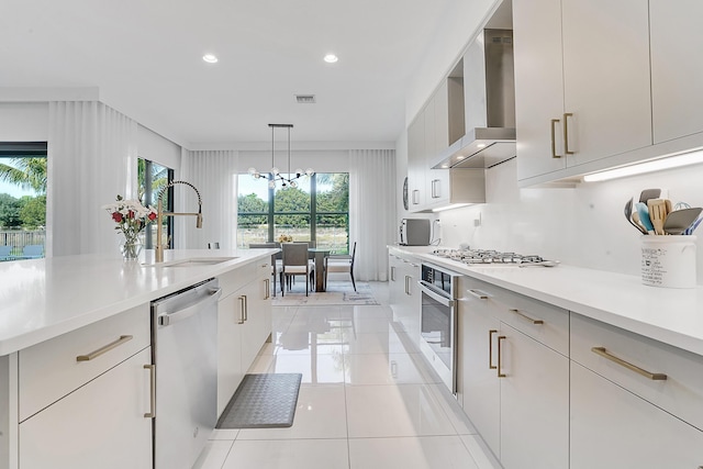 kitchen with sink, wall chimney range hood, a notable chandelier, decorative light fixtures, and appliances with stainless steel finishes