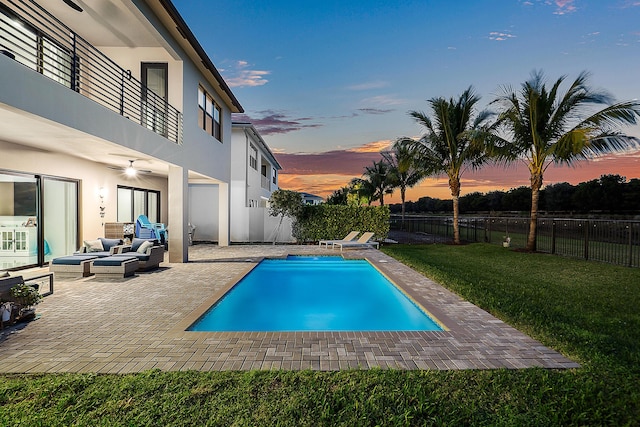 pool at dusk featuring an outdoor living space, ceiling fan, a yard, and a patio