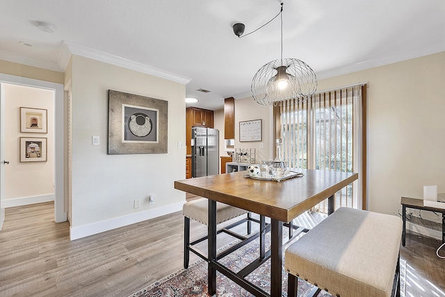 dining area with light hardwood / wood-style floors, crown molding, and a chandelier