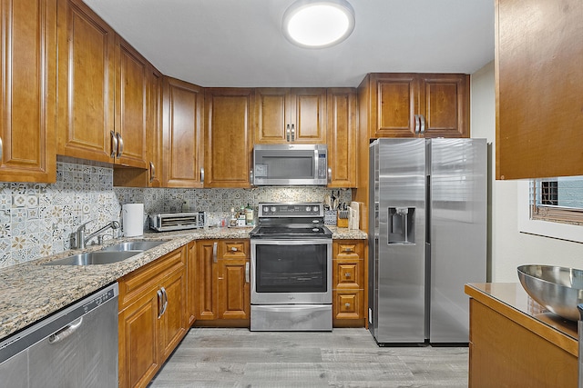 kitchen with appliances with stainless steel finishes, light wood-type flooring, backsplash, light stone counters, and sink