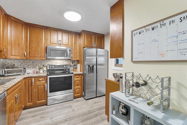 kitchen with decorative backsplash, light stone counters, stainless steel appliances, and light hardwood / wood-style flooring