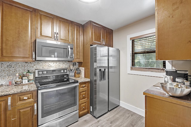 kitchen with backsplash, sink, light stone countertops, light wood-type flooring, and stainless steel appliances