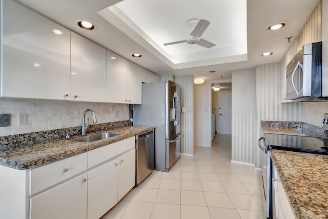 kitchen with ceiling fan, a raised ceiling, sink, white cabinetry, and stainless steel appliances