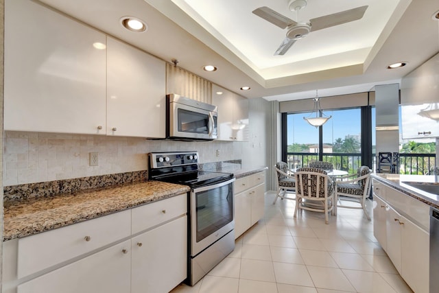 kitchen featuring white cabinetry, appliances with stainless steel finishes, backsplash, a tray ceiling, and hanging light fixtures