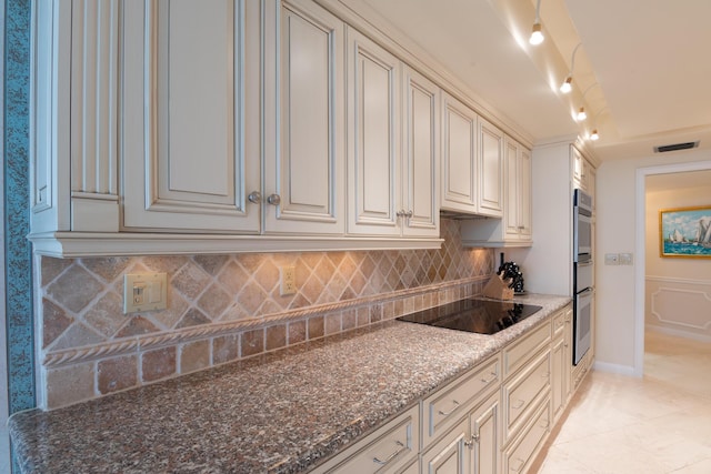 kitchen featuring cream cabinetry, stone counters, light tile patterned floors, black electric cooktop, and backsplash