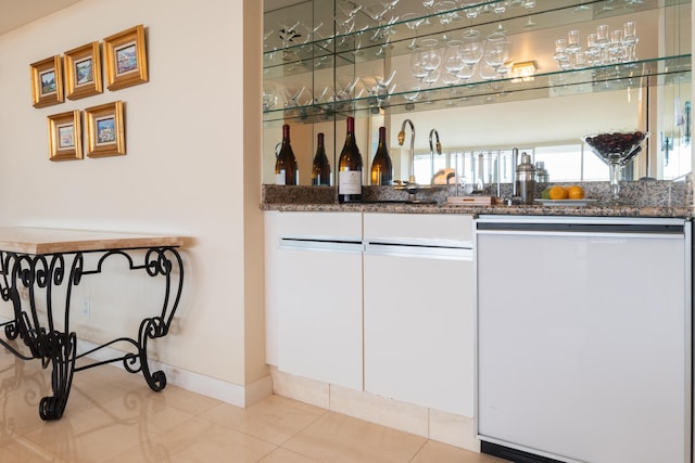 bar featuring white cabinets, dark stone counters, dishwasher, and light tile patterned floors