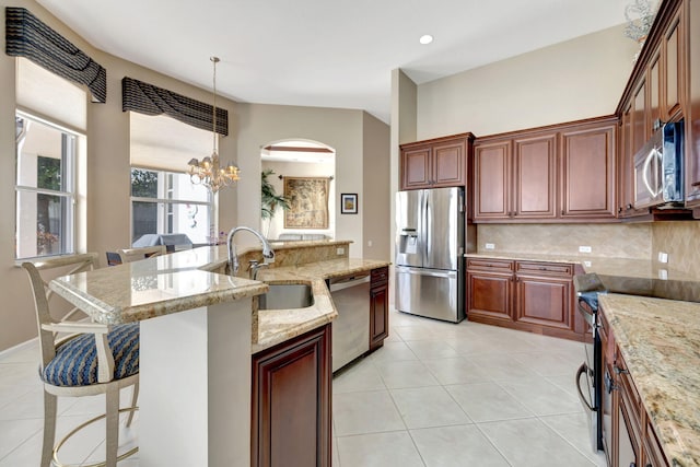 kitchen featuring light tile patterned floors, a breakfast bar area, stainless steel appliances, pendant lighting, and a sink