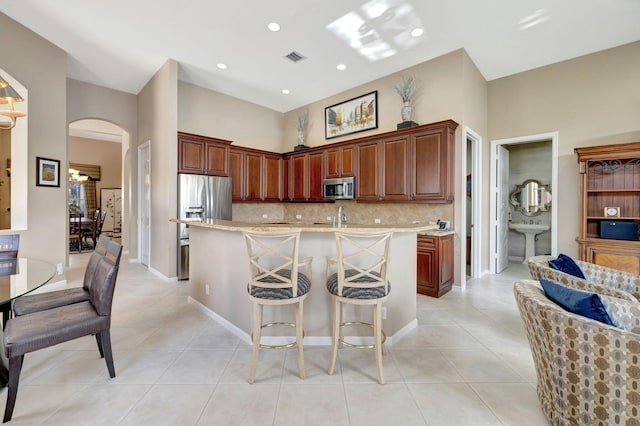 kitchen with light tile patterned floors, a breakfast bar, stainless steel appliances, a center island with sink, and decorative backsplash