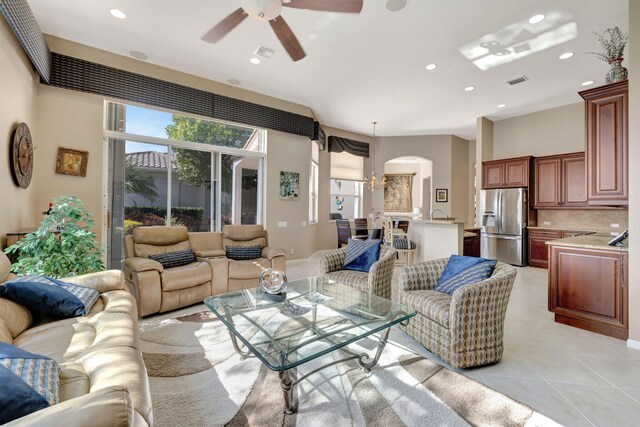 living area with ceiling fan with notable chandelier, arched walkways, visible vents, and light tile patterned floors