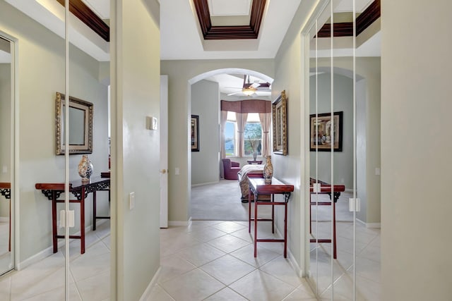 hall featuring arched walkways, light tile patterned floors, baseboards, a tray ceiling, and crown molding