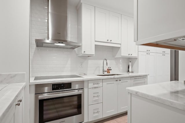 kitchen featuring stainless steel oven, sink, wall chimney exhaust hood, decorative backsplash, and white cabinetry