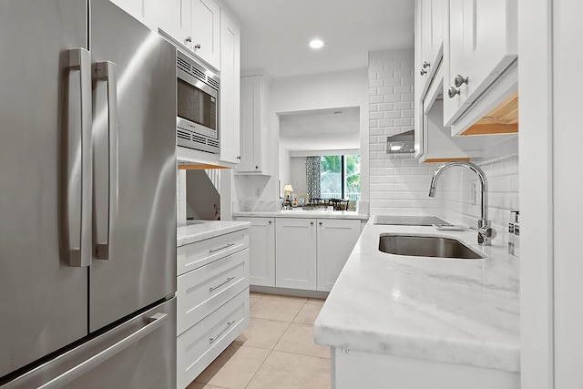 kitchen with appliances with stainless steel finishes, light stone counters, sink, white cabinetry, and light tile patterned flooring