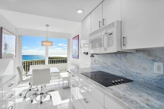 kitchen with a water view, hanging light fixtures, decorative backsplash, black electric cooktop, and white cabinetry