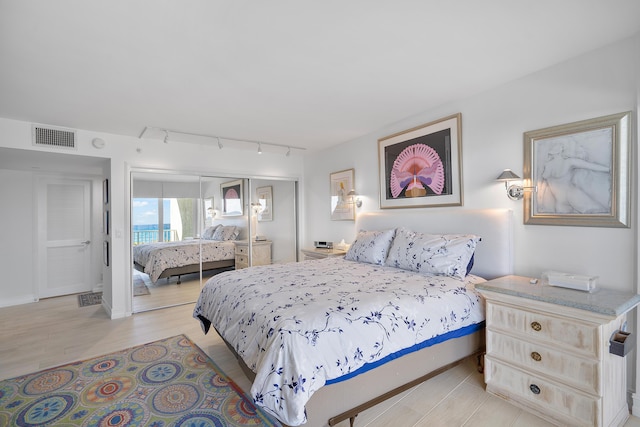 bedroom with a closet, track lighting, and light wood-type flooring