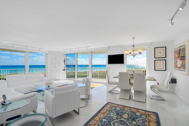 tiled living room with a notable chandelier, a water view, a wall of windows, and track lighting