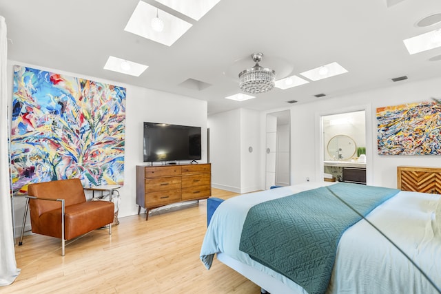 bedroom with ensuite bath, a skylight, a chandelier, and light wood-type flooring