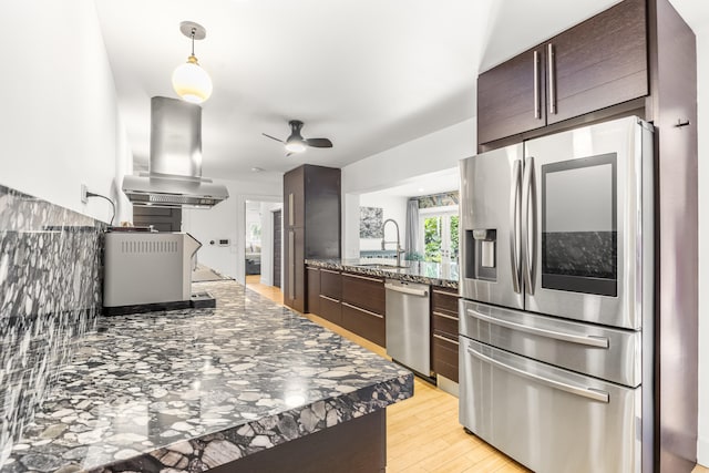 kitchen with sink, ceiling fan, dark stone countertops, appliances with stainless steel finishes, and island exhaust hood