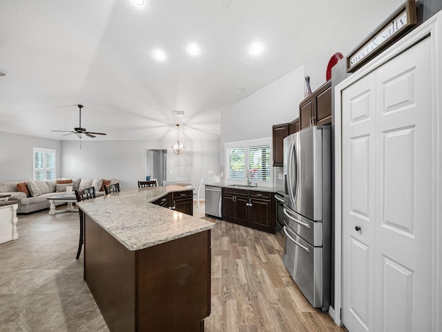 kitchen with stainless steel appliances, ceiling fan with notable chandelier, a wealth of natural light, hanging light fixtures, and a kitchen island