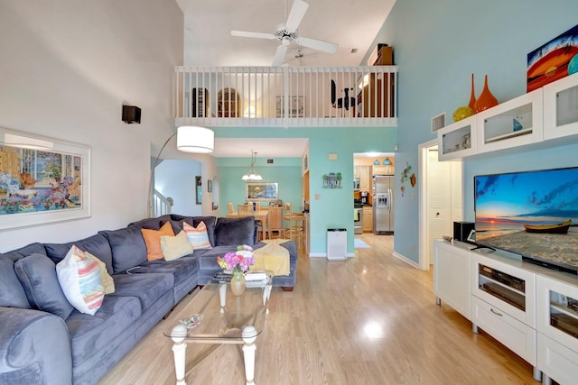 living room with light wood-type flooring, a towering ceiling, and ceiling fan