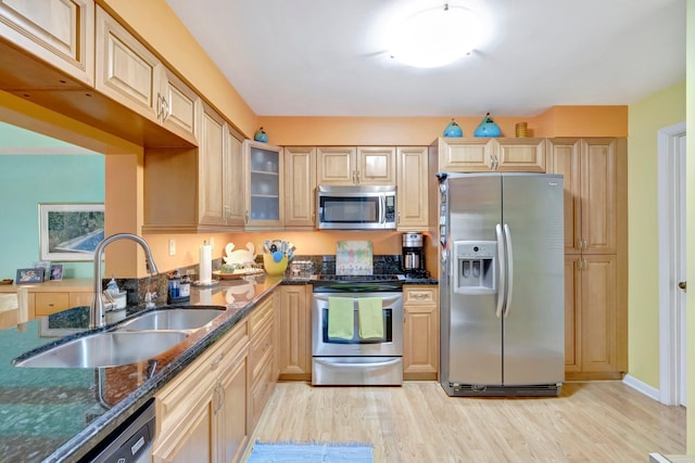 kitchen featuring sink, dark stone counters, light brown cabinetry, appliances with stainless steel finishes, and light wood-type flooring