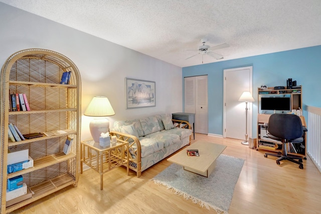 living room featuring ceiling fan, light hardwood / wood-style floors, and a textured ceiling