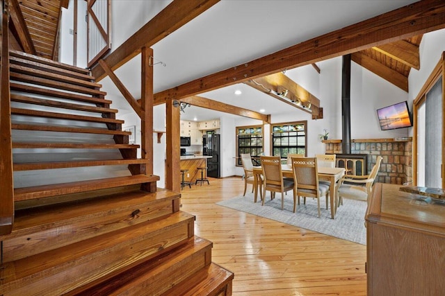 dining space featuring beamed ceiling, stairs, light wood-style flooring, a wood stove, and high vaulted ceiling