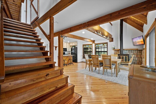 dining area featuring wood ceiling, a wood stove, high vaulted ceiling, beam ceiling, and light hardwood / wood-style flooring