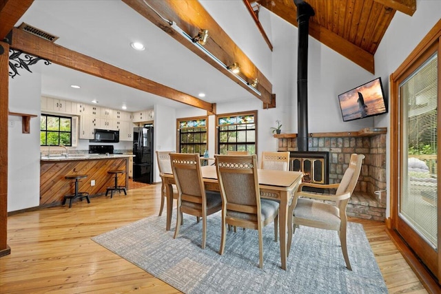 dining room featuring visible vents, beamed ceiling, a wood stove, and light wood finished floors