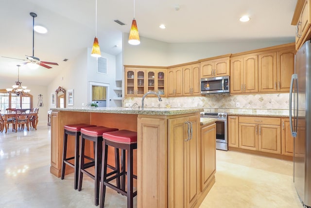 kitchen with decorative light fixtures, stainless steel appliances, tasteful backsplash, light stone counters, and a center island with sink