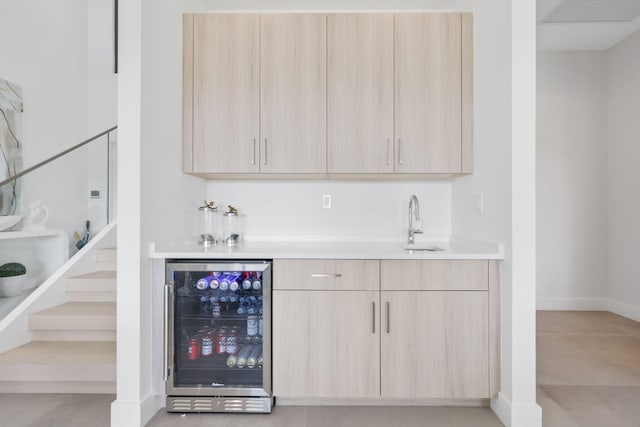 bar featuring light brown cabinets, beverage cooler, and sink