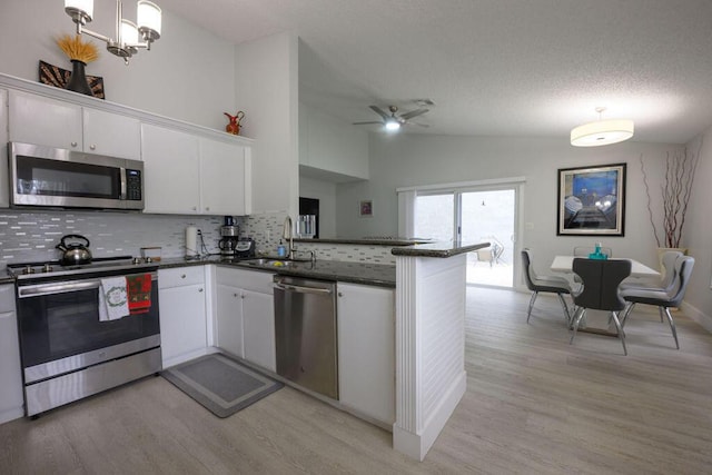 kitchen featuring stainless steel appliances, sink, white cabinetry, lofted ceiling, and kitchen peninsula