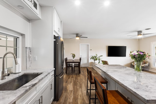 kitchen with white cabinets, light stone countertops, sink, and stainless steel refrigerator