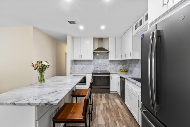 kitchen with appliances with stainless steel finishes, white cabinetry, and wall chimney range hood