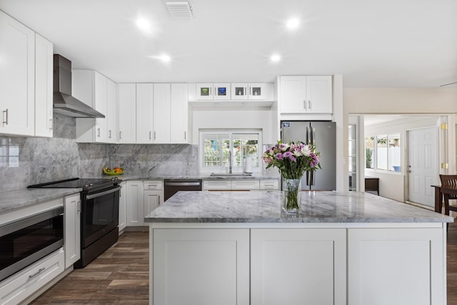 kitchen featuring white cabinets, a kitchen island, wall chimney range hood, and stainless steel appliances