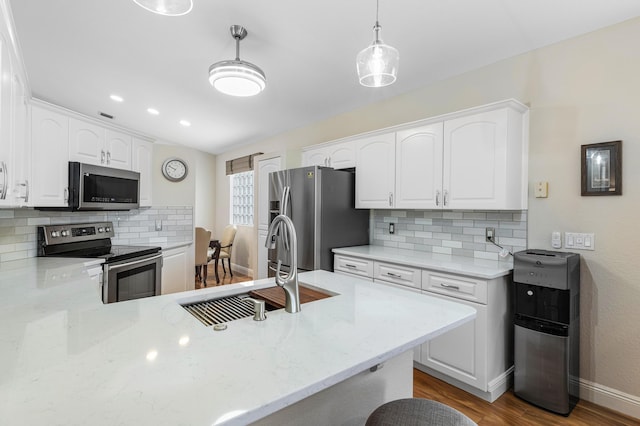 kitchen with a peninsula, wood finished floors, white cabinets, stainless steel appliances, and a sink