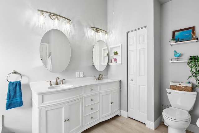 bathroom with double vanity, toilet, wood finished floors, and a sink