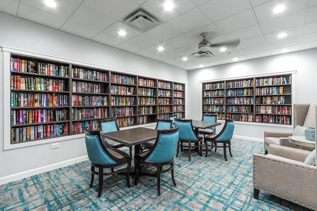 sitting room featuring wall of books, visible vents, carpet floors, and ceiling fan
