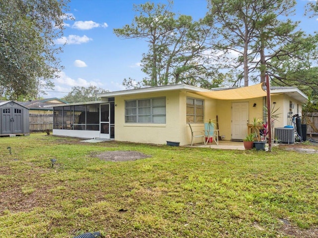 rear view of property featuring a sunroom, central air condition unit, a storage unit, and a lawn