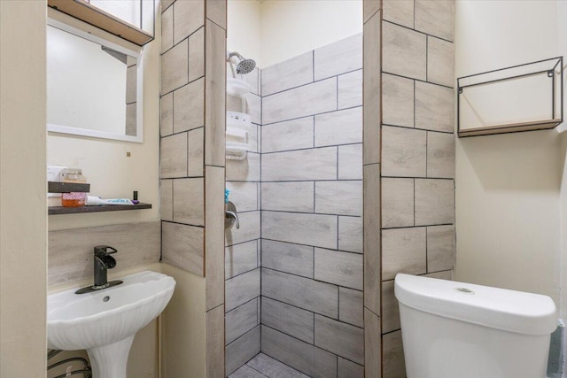 bathroom featuring tiled shower, toilet, and sink