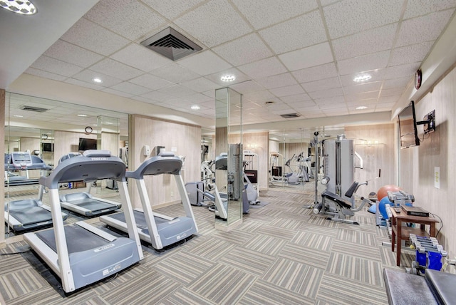 exercise room with a paneled ceiling, carpet, and wood walls