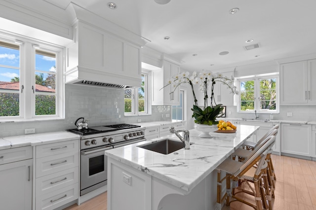 kitchen featuring a kitchen bar, a kitchen island with sink, sink, range with two ovens, and white cabinetry